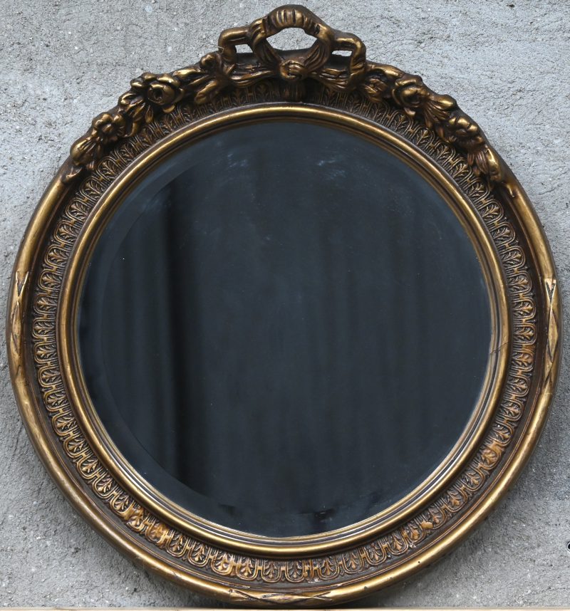 Een ronde spiegel met verguld kader en strikornament bovenaan.