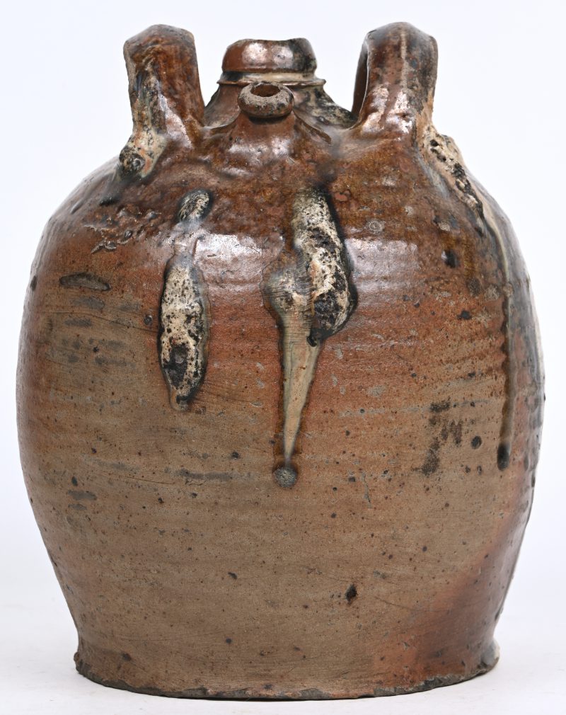 Een oude aardewerken schenkkan met 2 handvatten en schade aan de dop.