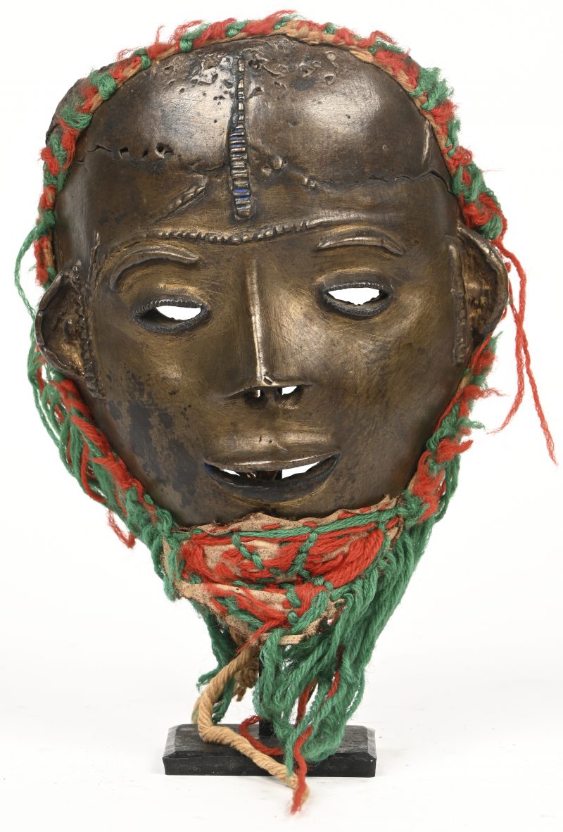 Een Afrikaans vrouwenmasker in brons met wollen versiering op metalen sokkeltje.