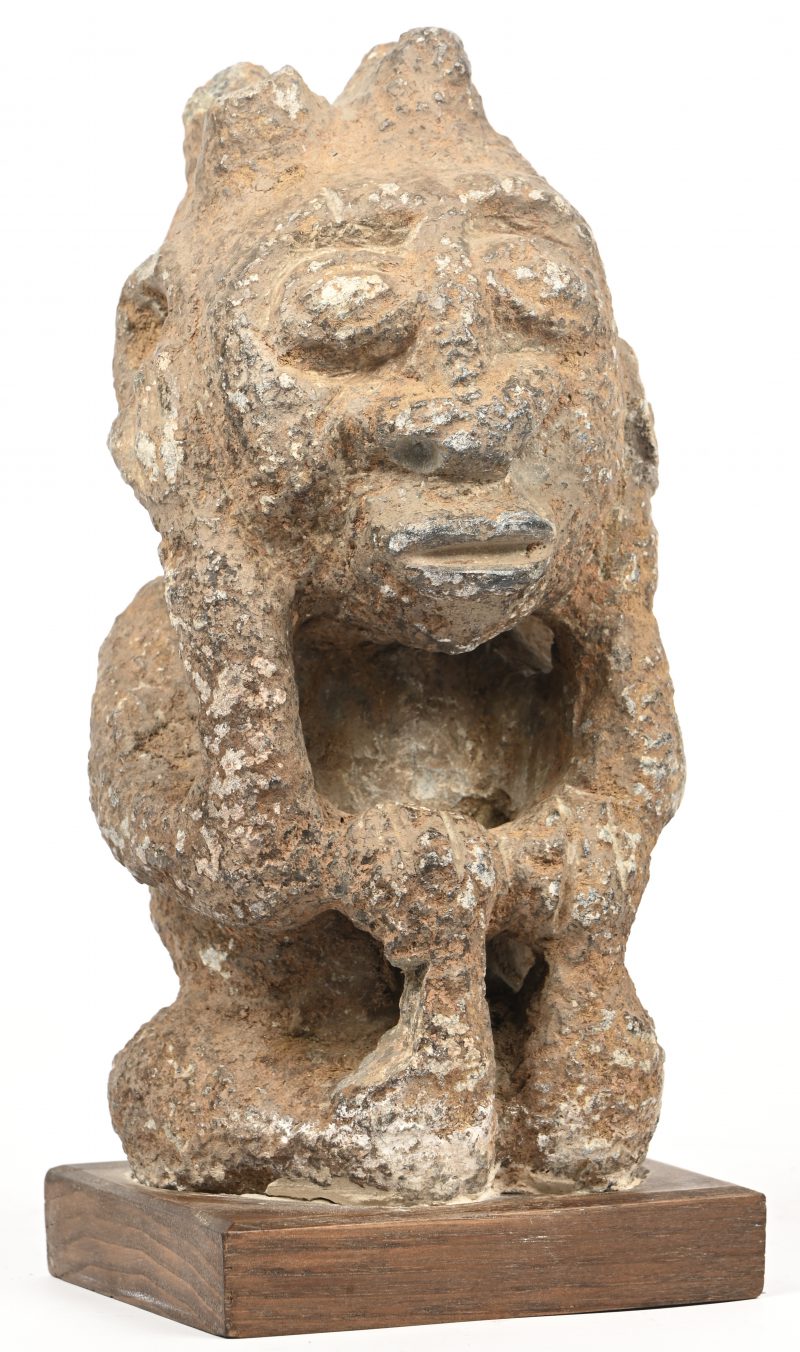 Een Afrikaans gebeeldhouwd stenen beeld van vermoedelijk een lokale godheid op een houten sokkeltje.