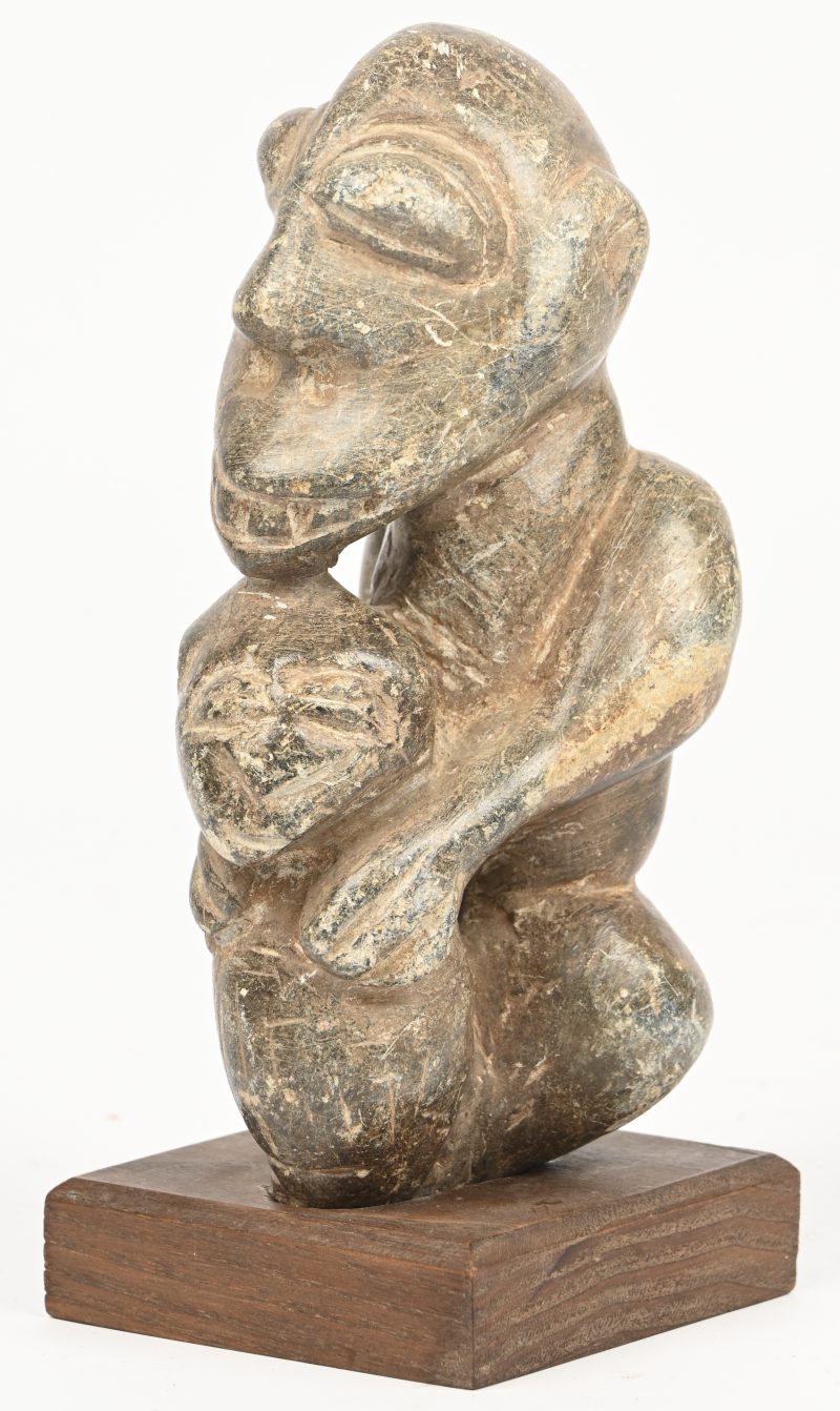 Een gebeeldhouwd Afrikaans stenen beeldje voorstellende een vader met kind op houten sokkeltje.