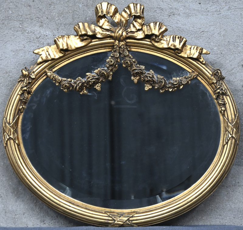 Een ovalen geslepen spiegel in vergulde kader m strik en guirlandes.