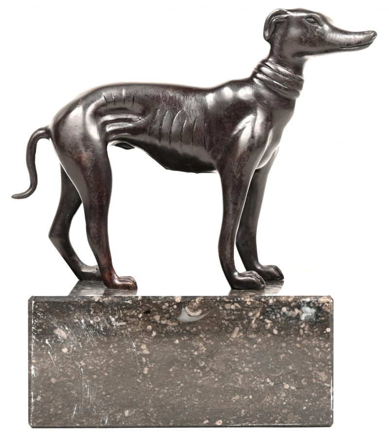 Een bronzen beeldje van een hond met zwart patina. Op een grijs marmeren sokkeltje.