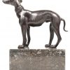 Een bronzen beeldje van een hond met zwart patina. Op een grijs marmeren sokkeltje.