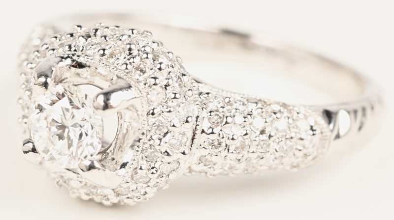 Een 18 karaats witgouden ring bezet met een centrale briljant van +- 0,44 ct. en briljanten met een gezamenlijk gewicht van +- 0,57 ct.
