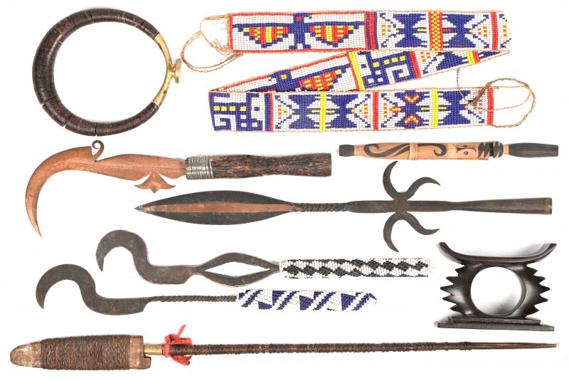 Een lot Afrikaanse werktuigen en sierraden bestaande uit enkele messen, speerpunt viersierd met kralen, een kralenband en een armband. Bijgevoegd een houten hoofd-neksteun.