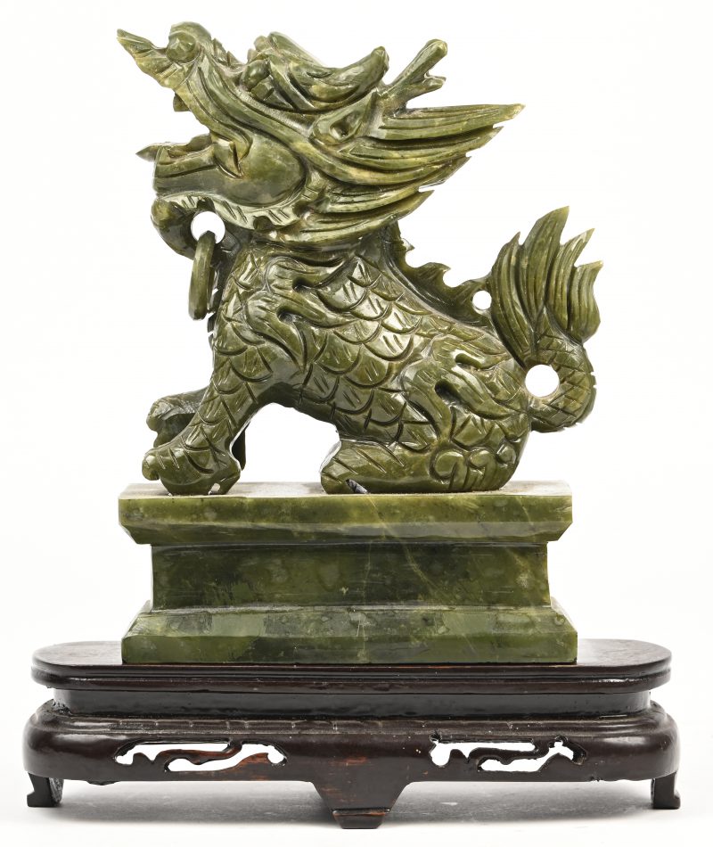 Een beeldje van een Chinese draak in speksteen op een houten sokkeltje.