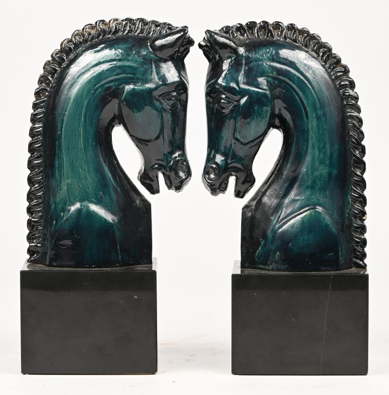 Een set groenblauwe keramische boeksteunen in de vorm van paardekoppen.
