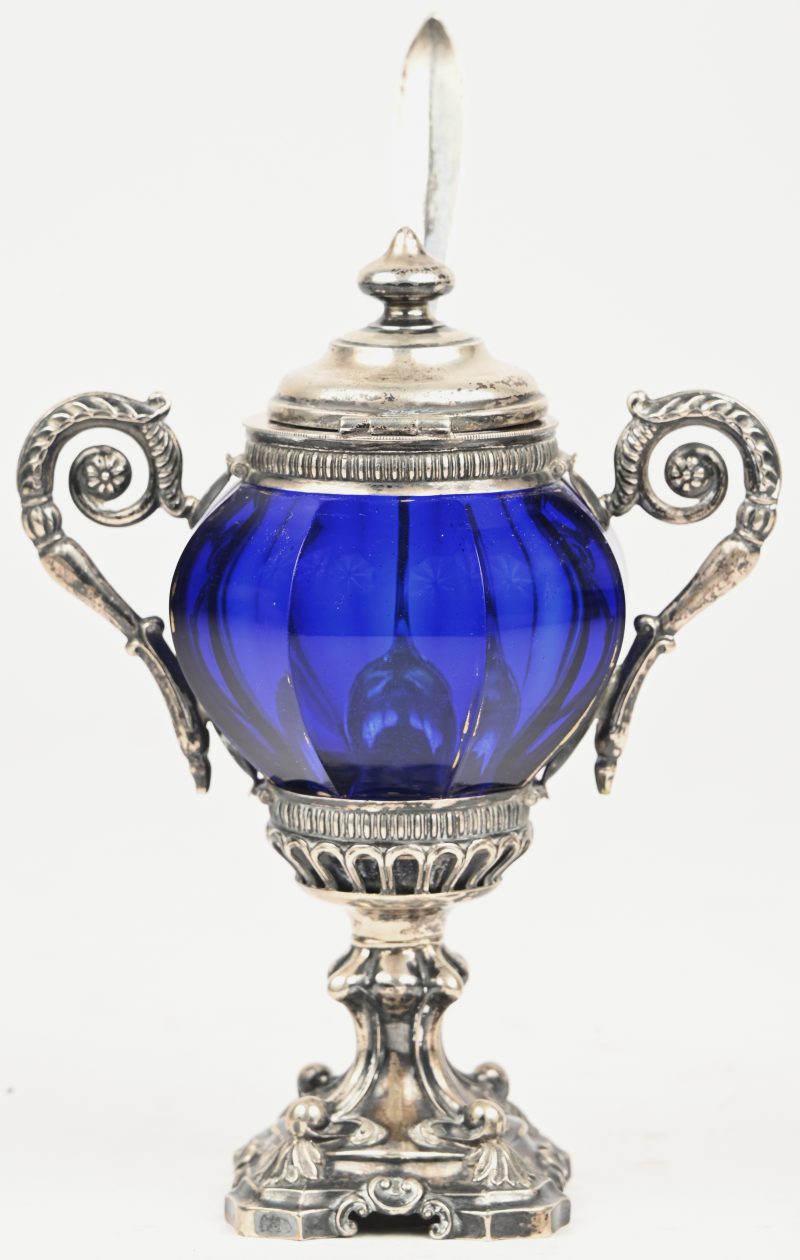 Een blauw glazen sauspotje met zilveren sculptuur en lepel.