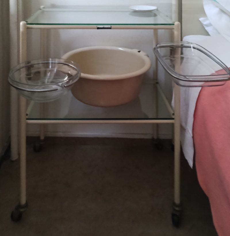 Een vintage medisch nachtkastje op wielen in glas en metaal met bijbehorende glazen kommen.
