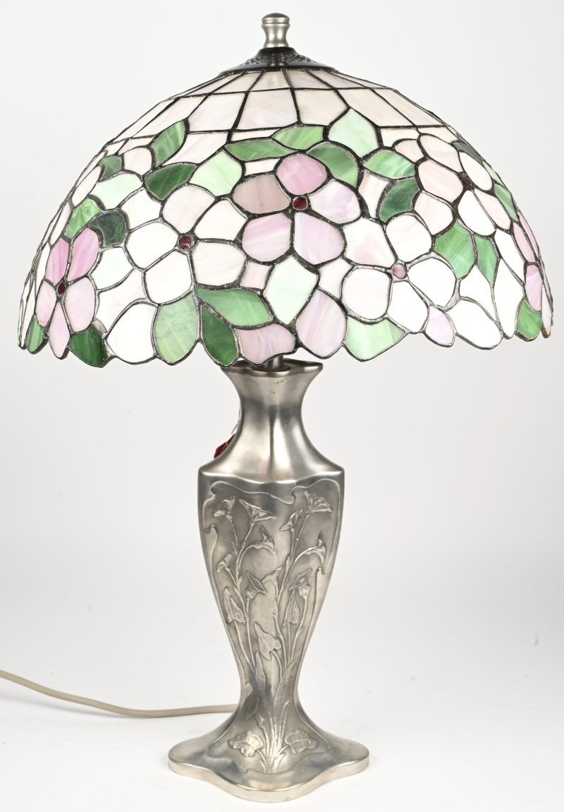 Een lampenvoet met een kap van glas in lood in de stijl van Tiffany. Gemerkt met label “Les etains des potstainiers hutois”.