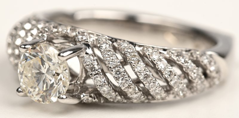 Een 18kt witgouden ring bezet met een centrale briljant 0,75 ct. J VS1 en bezet briljanten met een gezamenlijk gewicht van 0,55 ct.