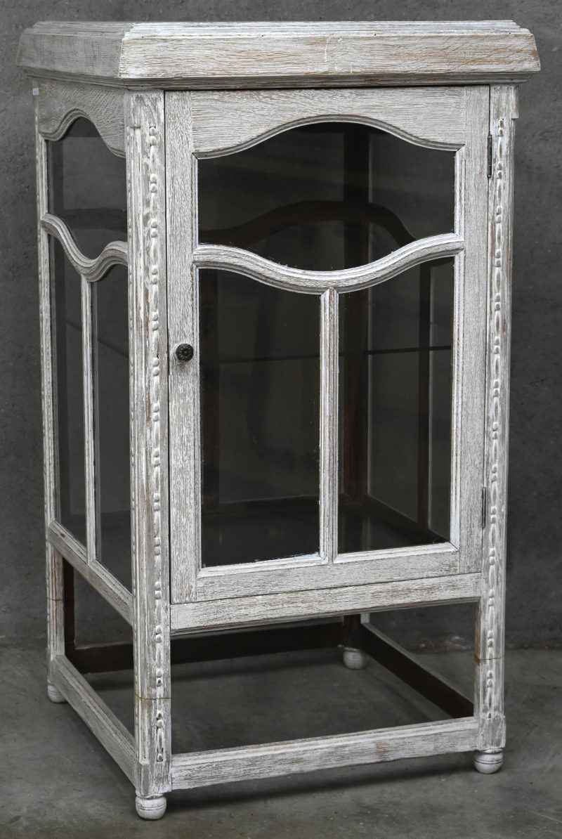 Een whitewashed houten vitrinekast met deur en 2 niveau’s.