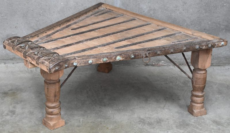 Een Indiase houten salontafel met blad in trapeziumvorm op 3 poten. Met metalen strips belegd en gesculpteerde details in het decor.
