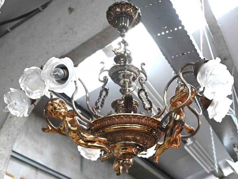 Een bronzen luchter met 3 engelen, met 9 lichtpunten en glazen blakers in de vorm van roosjes.