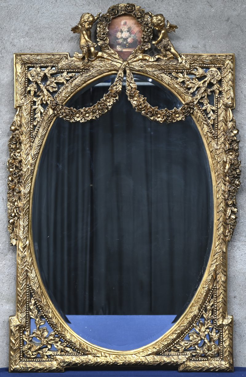 Een ovalen spiegel met een goudkleurige kader in kunststof met engeltjes en guirlandes.