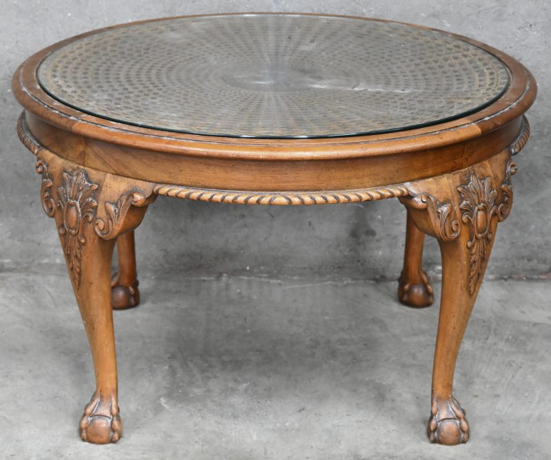 Een houten ronde salontafel met glazen blad en vlechtwerk op leeuwenpoten voet.