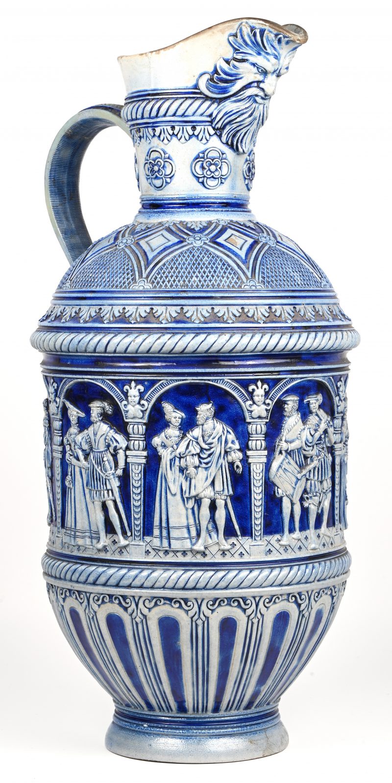 Een Duits aardewerken schenkkruik. Kobalt blauw met diverse figuur taferelen in het reliëf en gezicht met baard aan de teut. Westerwald steengoed, 19e eeuws.