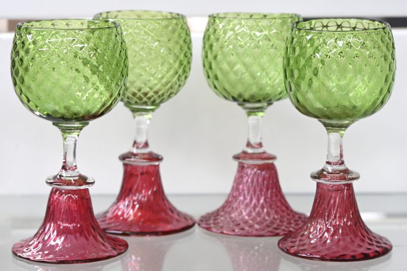 Een set van vier kristallen glaasjes met groene kelk en rode voet.