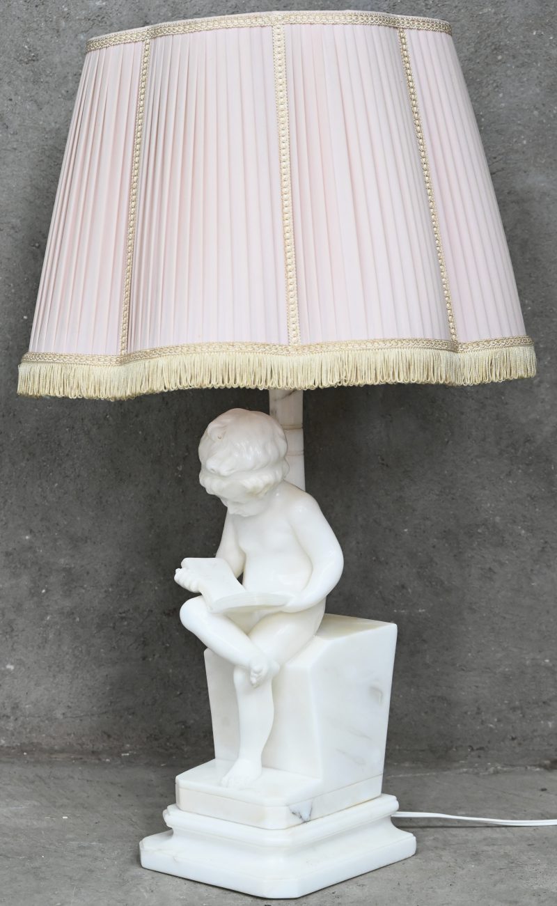 Een tafellamp met als voet een marmeren lezend kindje met bijhorende roze kap.