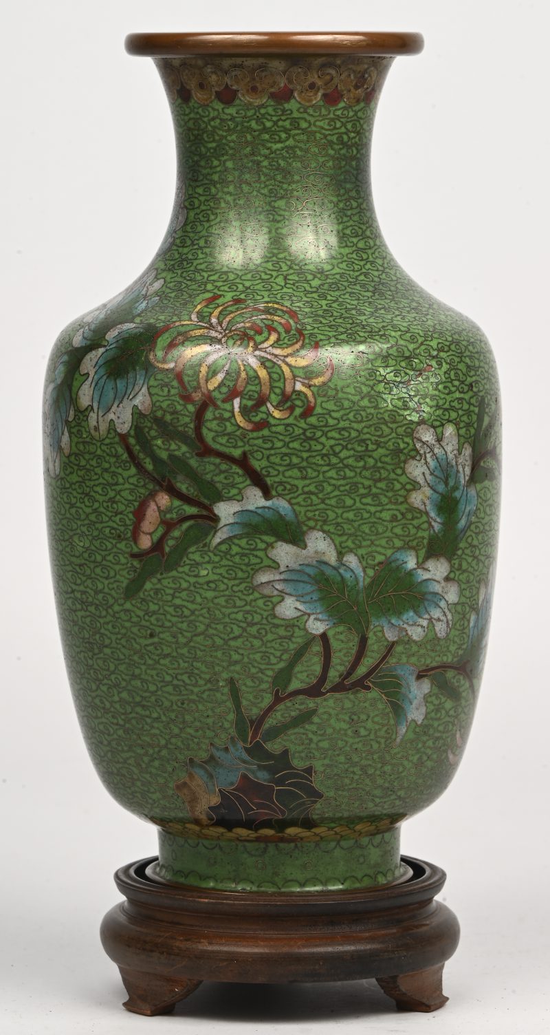 Een Chinese cloisonné vaas, groenkleurig met floraal decor, op houten sokkel. Deukje in zijde aanwezig.