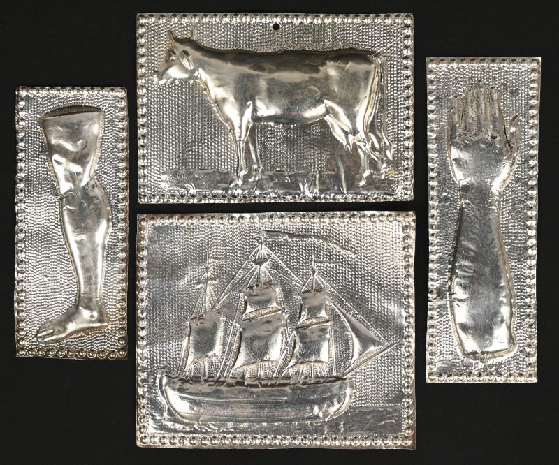 Een lot van vier zilveren ‘ex-voto’s’, een arm, een been, een koe en een driemaster.