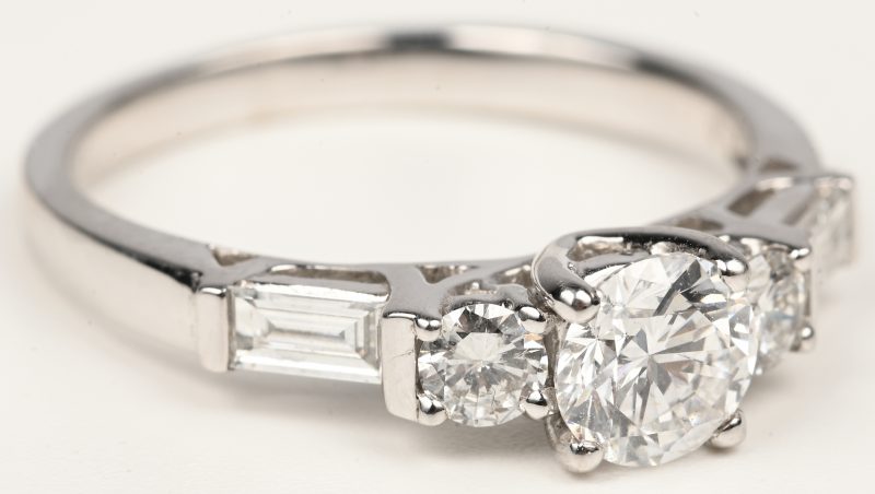 Een 18 kt witgouden ring bezet met een centrale briljant van +- 0,61 ct. FVS1 en diamant baguetten en briljanten met een gezamenlijk gewicht van +- 0,43 ct.