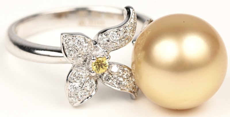 Een 18 kt witgouden ring bezet met briljanten in strikvorm met een gezamenlijk gewicht van +- 0,30 ct. en een goudkleurige parel.