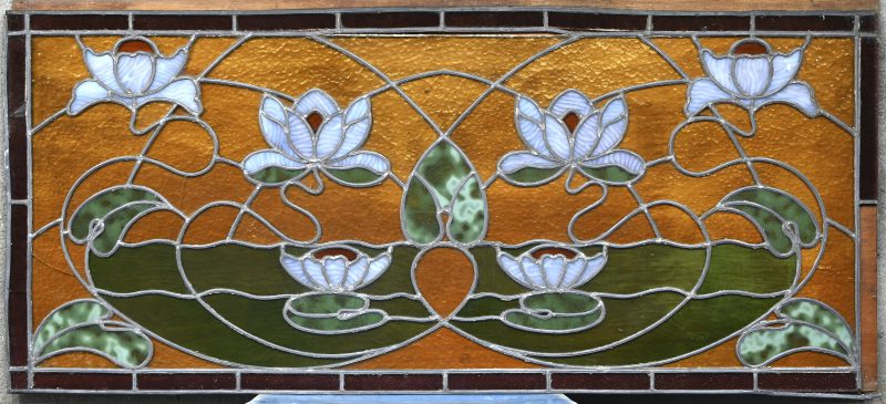 Een langwerpig glas-in-loodraam, periode interbellum met floraal decor. Eén korte kant beschadigd.
