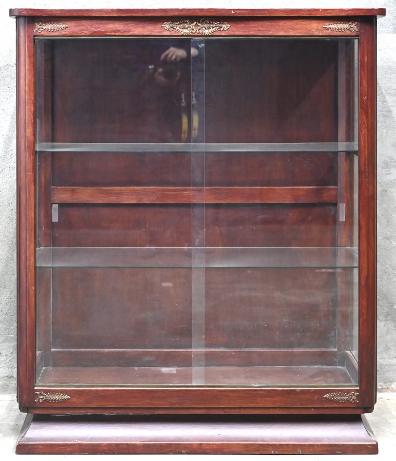 Een houten vitrinekast met glazen schuifraam en 2 verdiepen en koperen beslag.
