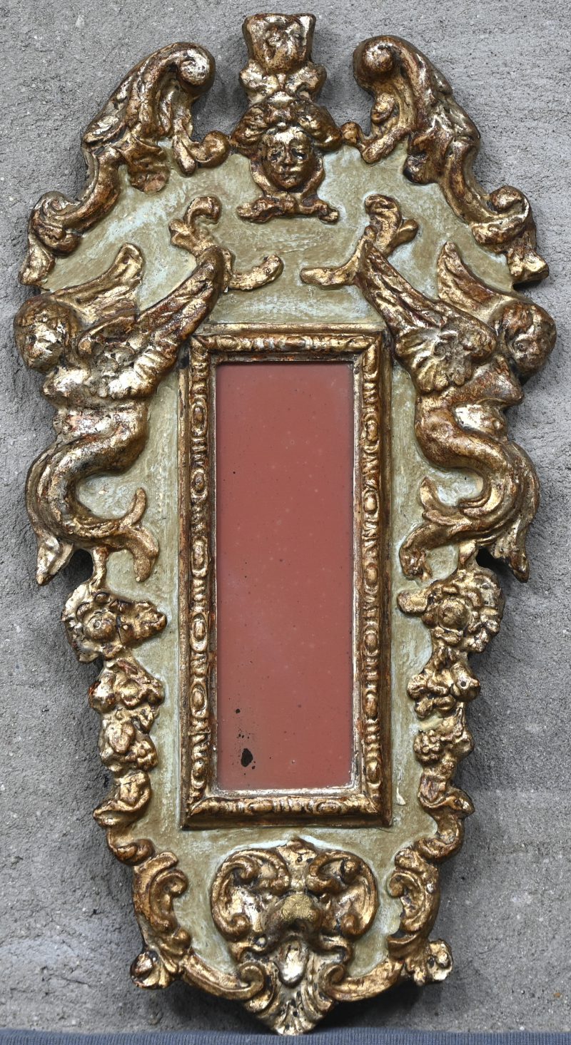 Een gepatineerd hout gesculpteerd spiegelkader met divers decor in het reliëf. Made in Italy.