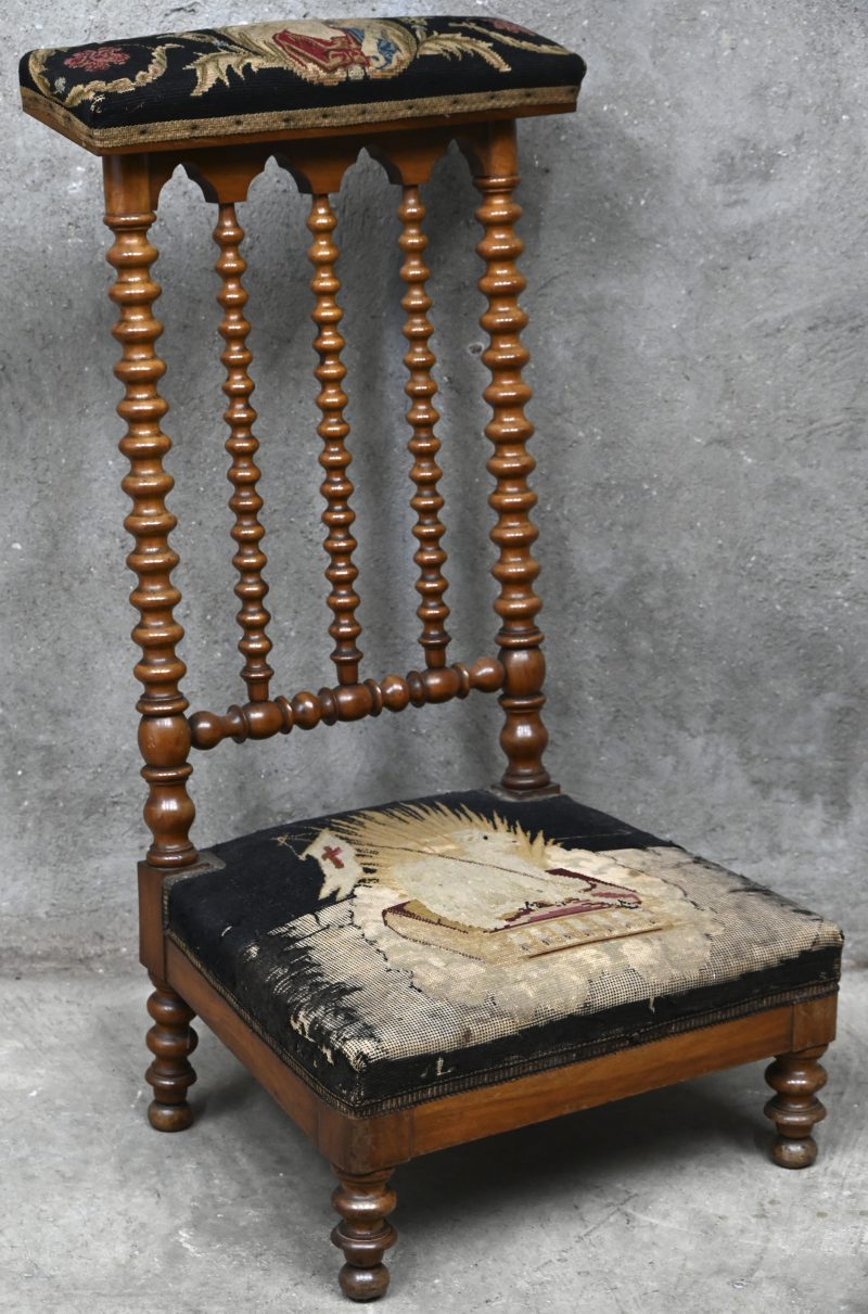Een 19e eeuwse bidstoel met een versleten gobelin zitting met de afbeelding van het Lam Gods en bovenop de leuning de afbeelding van een apostel.