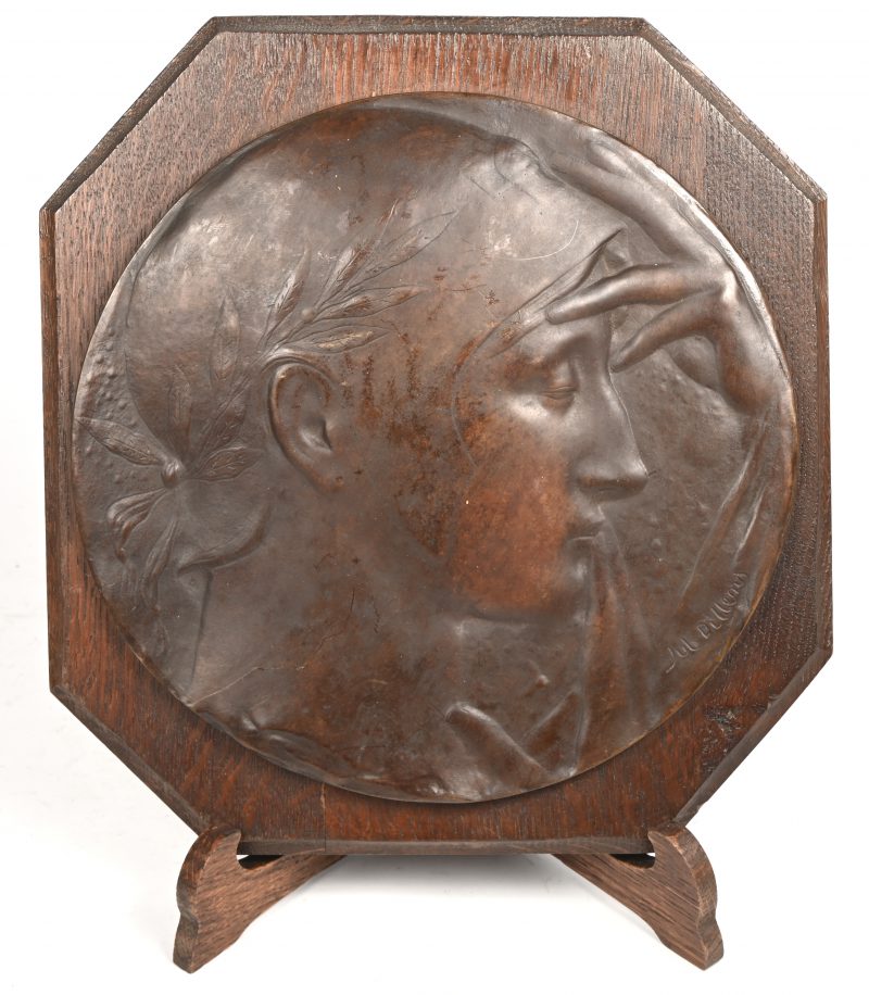 Bronzen profiel met laurierkrans op houten plaquette, draagt handtekening Jul Dillens.