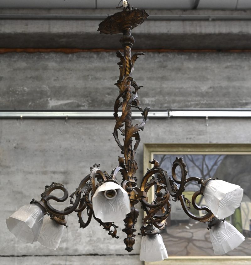 Een brons gesculpteerde luchter met 6 lichtpunten en melkglazen kapjes. Organisch gevormde armen.