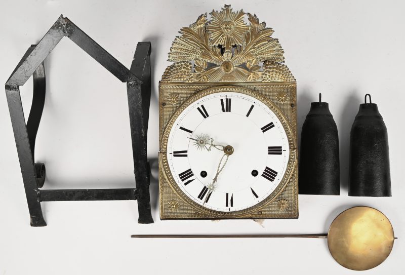 Een comtoise klok met opschrift ‘Hora Fugit’ met emaille wijzerplaat en een versiering in Dinanterie.