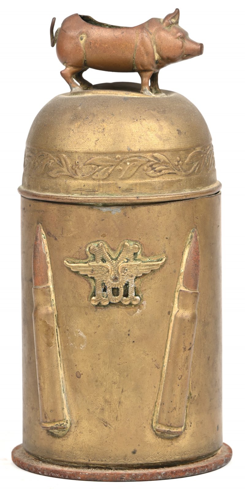 Een trench-art obus met een deksel waarop een zwijntje, een militair embleem en 2 kogels vooraan.
