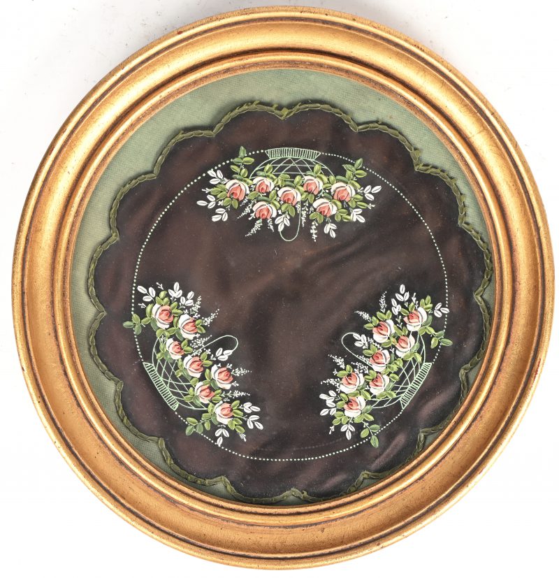 Een rond verguld kader met beschilderd zijden onderlegger met florale elementen.
