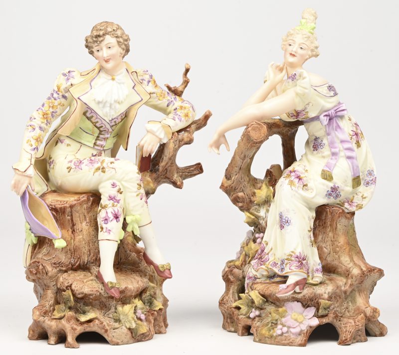 Een set van 2 handbeschilderde beeldjes van een edelman en jonkvrouw gezeten op een boomstronk. Dragen een merkje en een nummer in de voet.