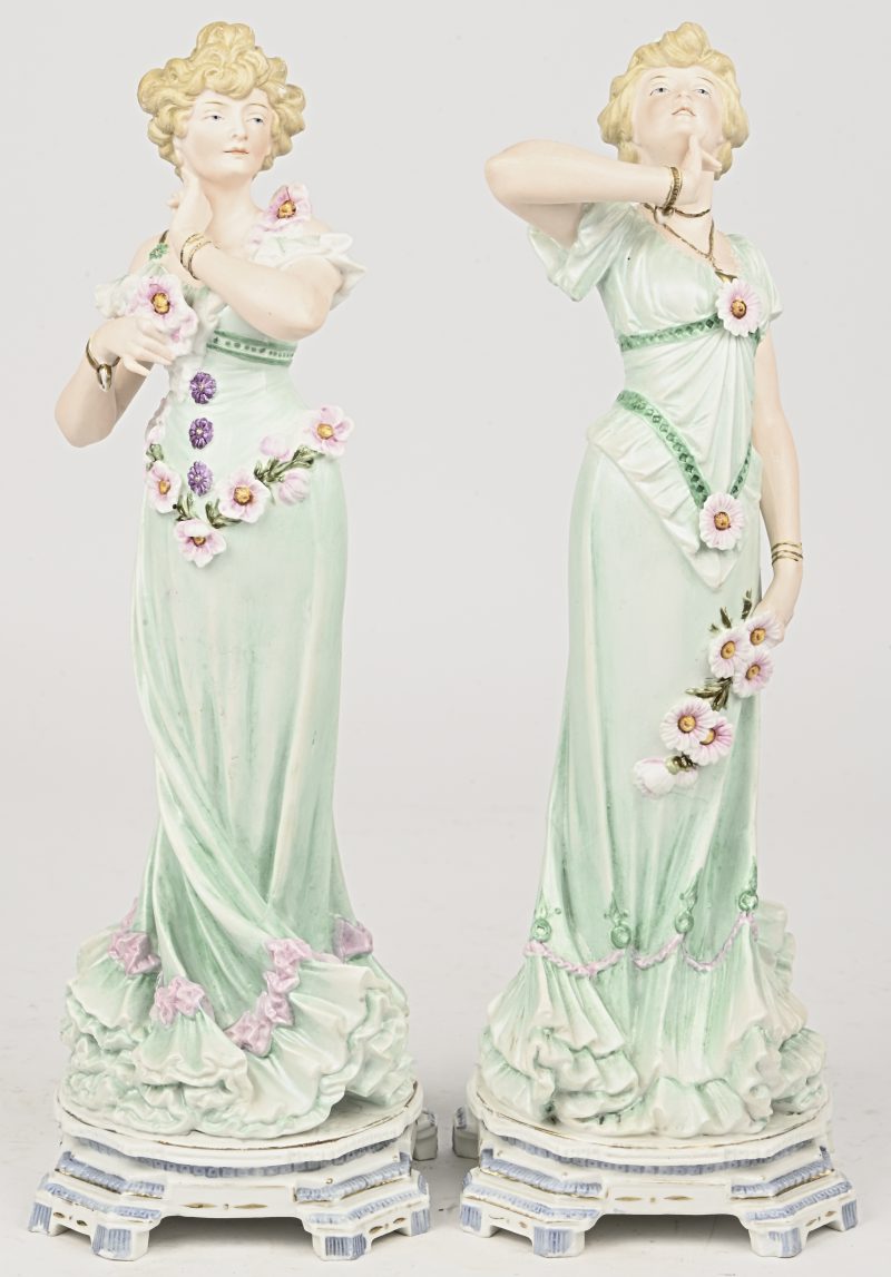 Een paar polychroom biscuit beeldjes van twee romantische dames met lichtgroene kleding met bloemen.