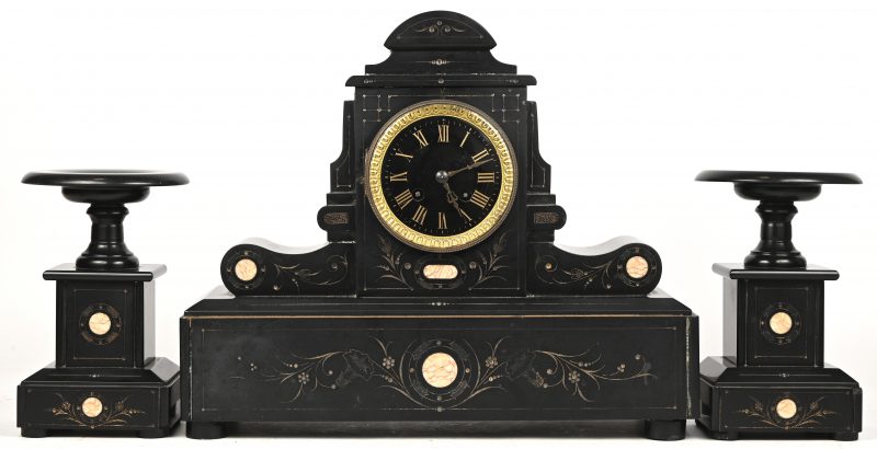 Een driedelig schouwstel van zwart marmer met gravures in  het decor, bestaande uit een pendule en twee cassolettes. Met slinger en sleutel. Eind 19e eeuw.