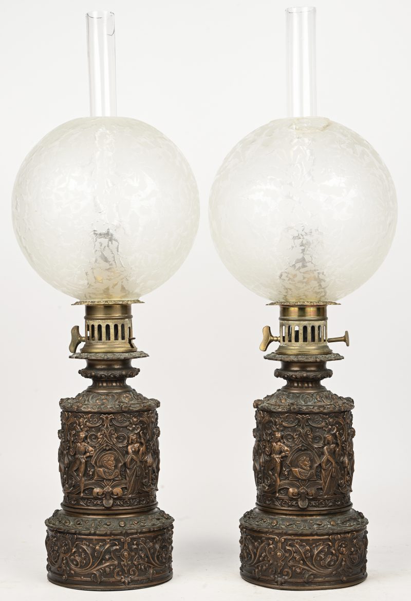 Een paar koperen petroleum lampen met glazen bol en hoftafereel in het reliëf. Barst in 1 bol en 1 bovenaan in glazen wiekglas.
