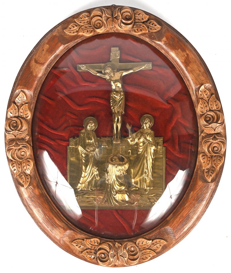 “Jezus aan het kruis”. Een messing reliëf beeld onder convex glas in ovalen houten kader met gesculpteerd florale details.