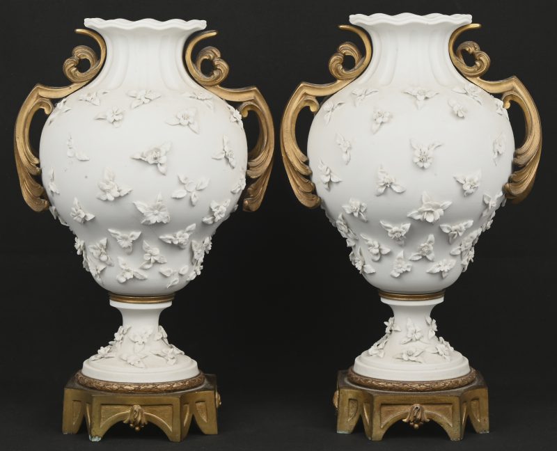Een set van 2 biscuit vaasjes met een decor van bloemen en verguld bronzen ornamenten en voet. Aan beide vaasjes is er schade aan de bloemen. Onderaan dragen ze het merkteken van Sèvres.