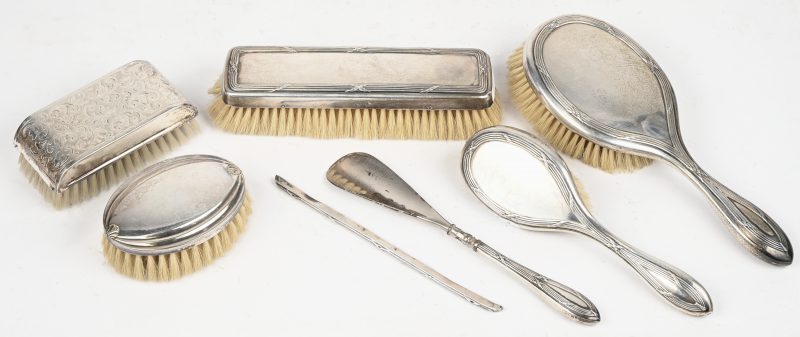 Een zilveren set bestaande uit 3 borstels, een schoenlepel en het zilveren deel van een kam. Alle 5 delen dragen de stempel van Delheid. Toegevoegd 2 borstels met verzilverde houder.