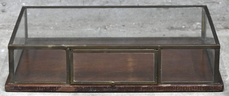 Een vintage glazen toogvitrine met messing frame en 1 klepje vooraan. Glas achterzijde manco. Bovenzijde glas gemerkt.