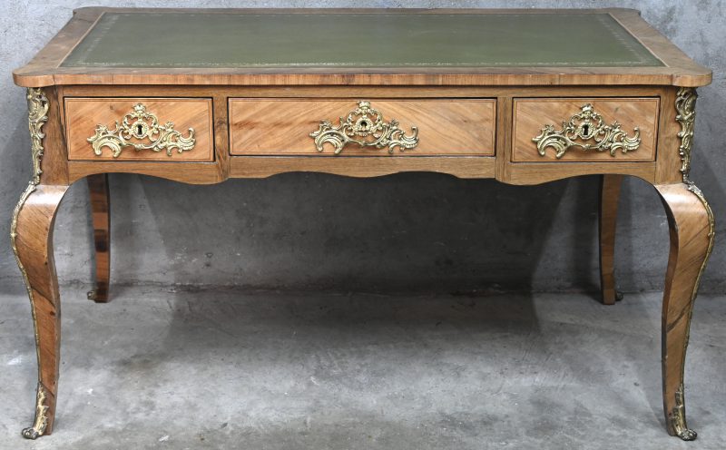 Een bureau in Louis XV-stijl in gefineerd notelaar. 3 lades en 3 valse lades en groen lederen blad. Vergulde bronzen beslag.