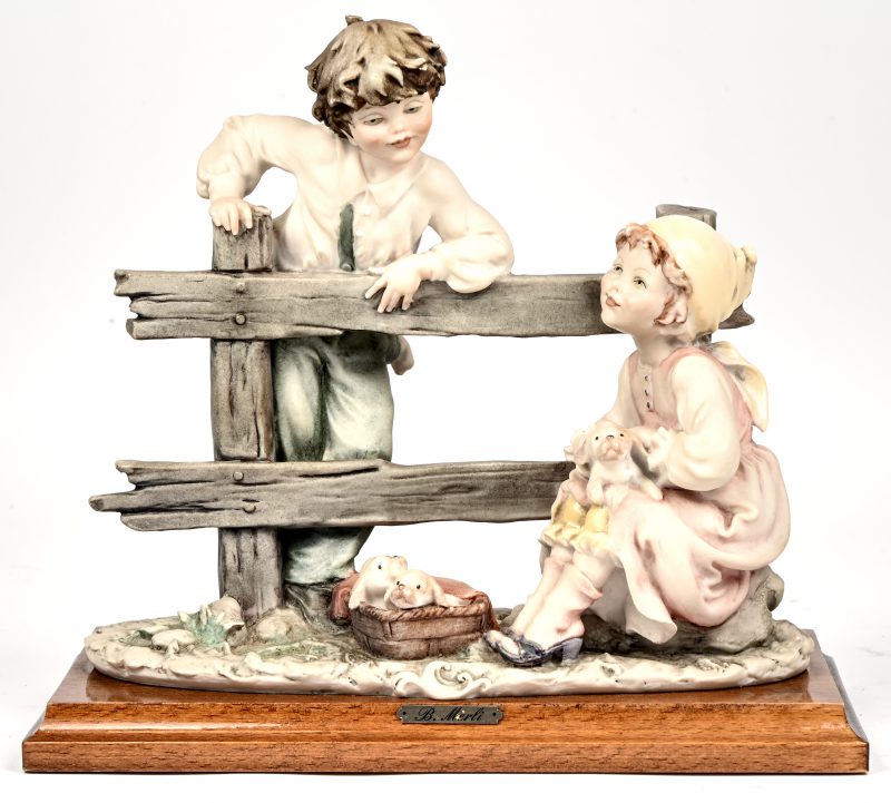Een Capodimonte beeldje van een jongen en een meisje aan een hek met puppy’s.