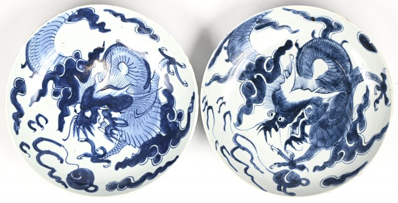 Een set van 2 blauw-witte Chinese borden met drakendecor. Het ene bord heeft een bakfoutje en het andere een haarlijnscheurtje, beide met kleine schilferschade.
