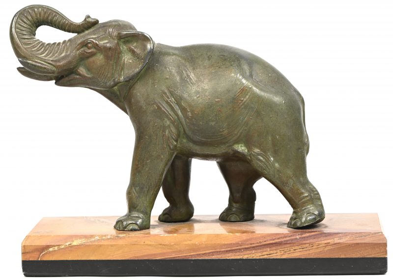 Een beeldje van een olifant in zamak, groene patine, op een marmeren voet. De rechter achterpoot vertoond een barst.