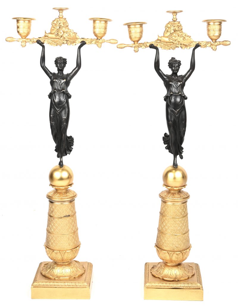 Een paar kandelaars in Empire stijl van verguld en gepatineerd brons, gedragen door vrouwenfiguren.
